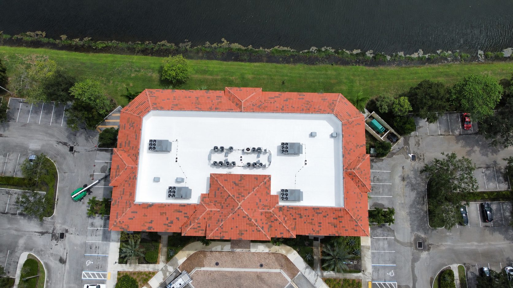 Top-down drone view of a commercial building with a clean white flat roof and clay tile edges after soft wash roof cleaning