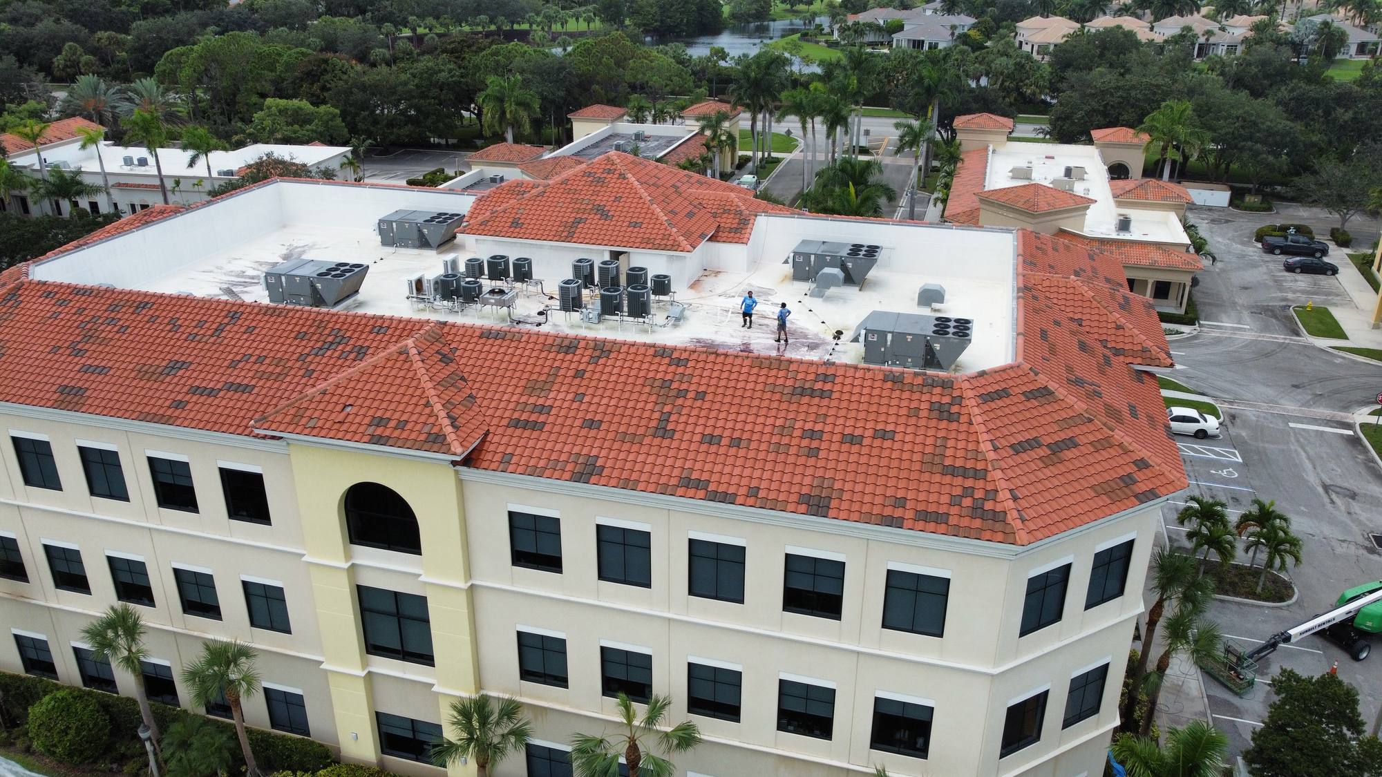 Aerial view of a cleaned low-slope commercial roof beside terra cotta tile