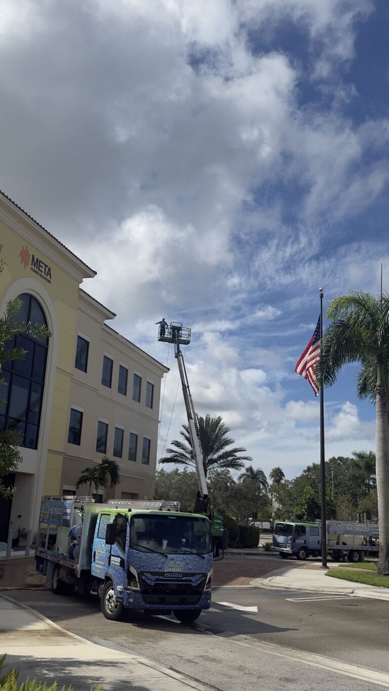 Aqua Force trucks and a boom lift at a commercial building while a technician cleans the roofline